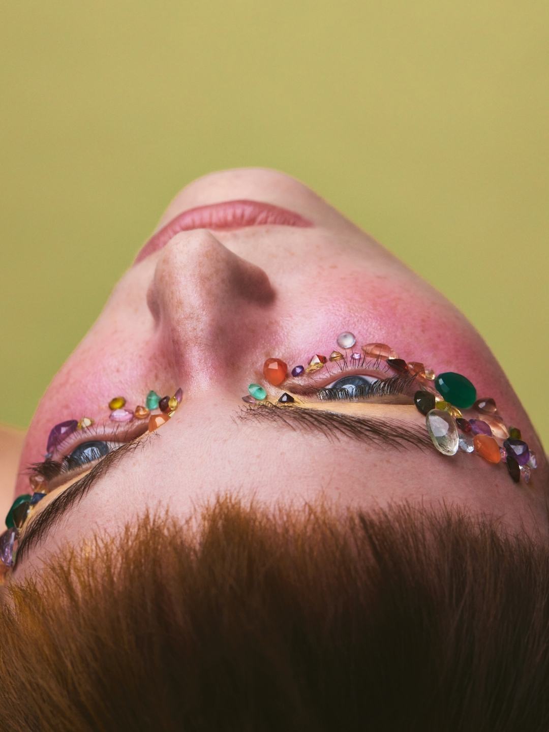 Close-up portrait of a person from below with colorful gemstone crystals glued around their eyes.