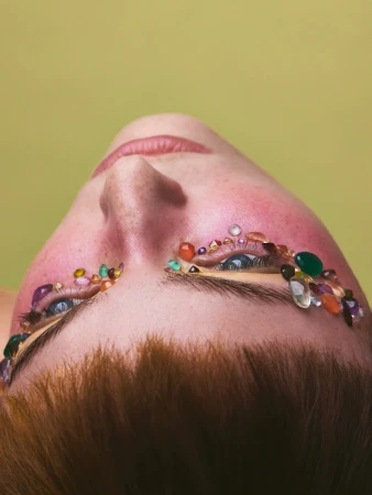 Close-up portrait of a person from below with colorful gemstone crystals glued around their eyes.