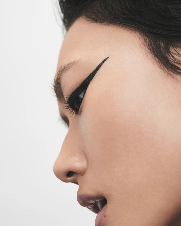 Close-up profile of a model featuring sharp winged black eyeliner against a plain white background