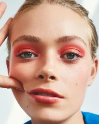 Close-up portrait of a model with vibrant red eyeshadow and fingers pressing into cheek, photographed by Joshua Pestka