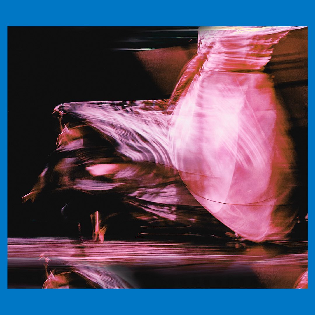 Abstract blurred image of a person in motion with pink fabric against a dark background, creating a sense of movement and energy.