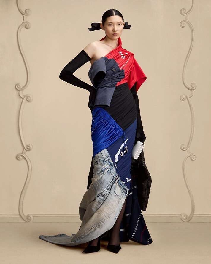 Fashion model poses in a full-length shot, wearing a unique dress made of repurposed clothing materials, in a studio setting.