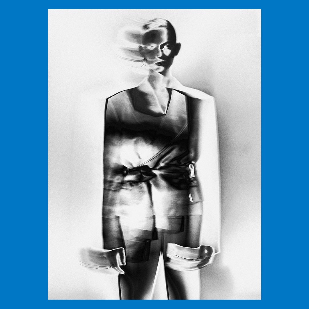 Abstract monochrome studio portrait of an adult female model wearing a suit with a blurred effect, against a clean white background.