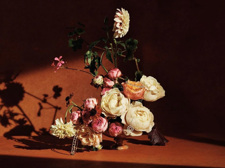 Dramatic floral arrangement featuring roses and dahlias in warm, muted tones, set against a textured, earthy background.