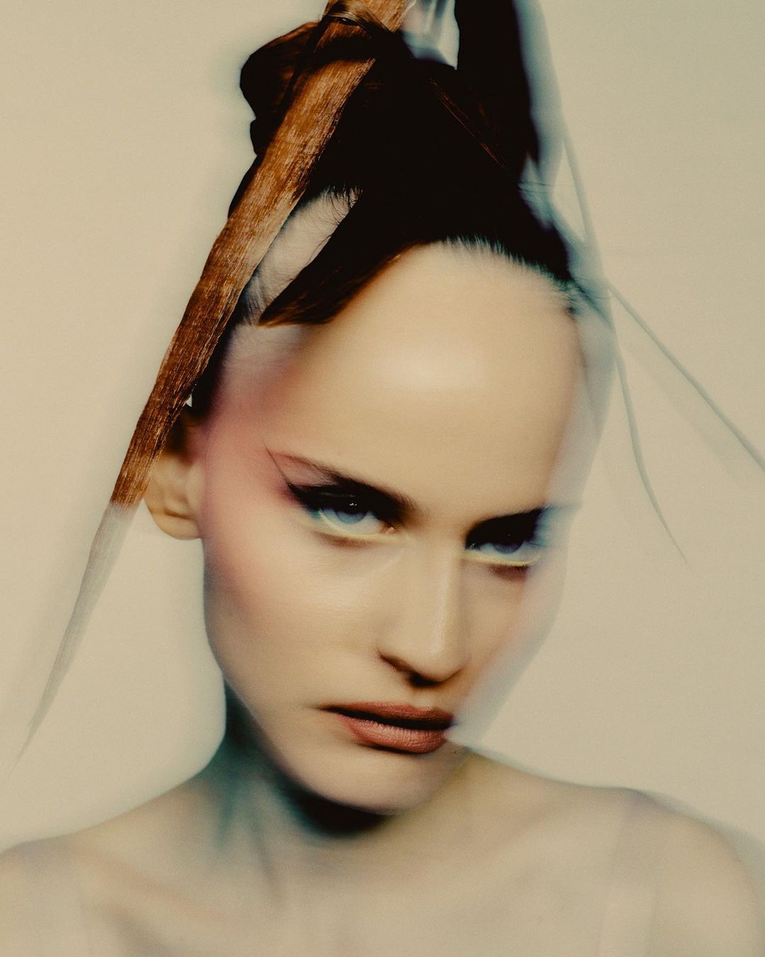 Close-up beauty portrait of a woman with fair skin, dark hair styled up, and dramatic eye makeup, with a blurred, dreamy aesthetic.