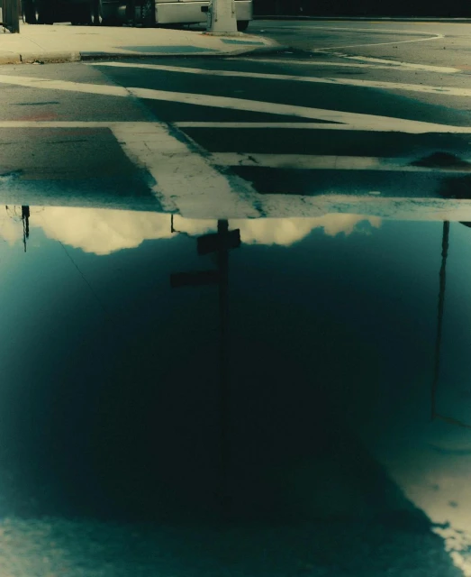 Street scene with crosswalk reflection in a puddle. Urban scene shows asphalt road with white stripes, and sky and street pole reflection.
