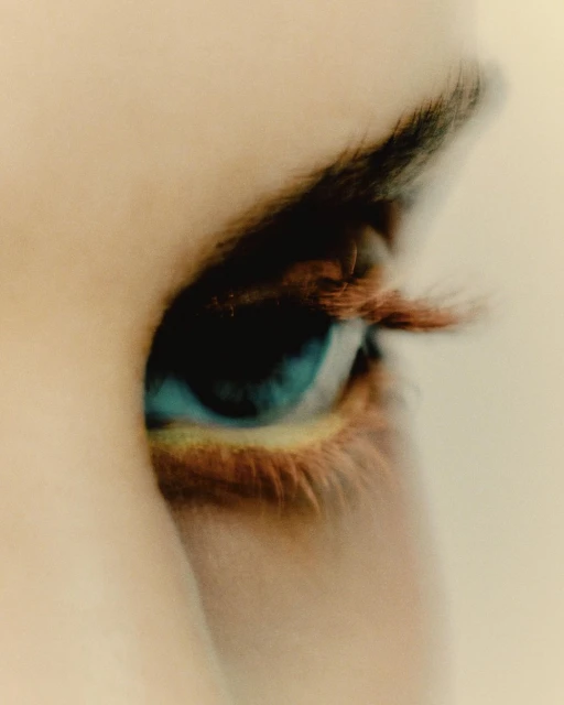 Macro, blurred, close-up shot of a person's eye. The eye features a blue iris, brown eyelashes, and a soft skin tone.