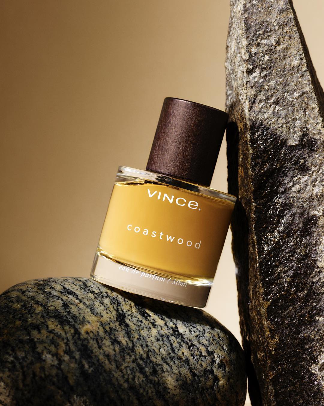 Vince Coastwood fragrance bottle sitting on rocks, product shot for beauty and personal care, neutral beige background with text.