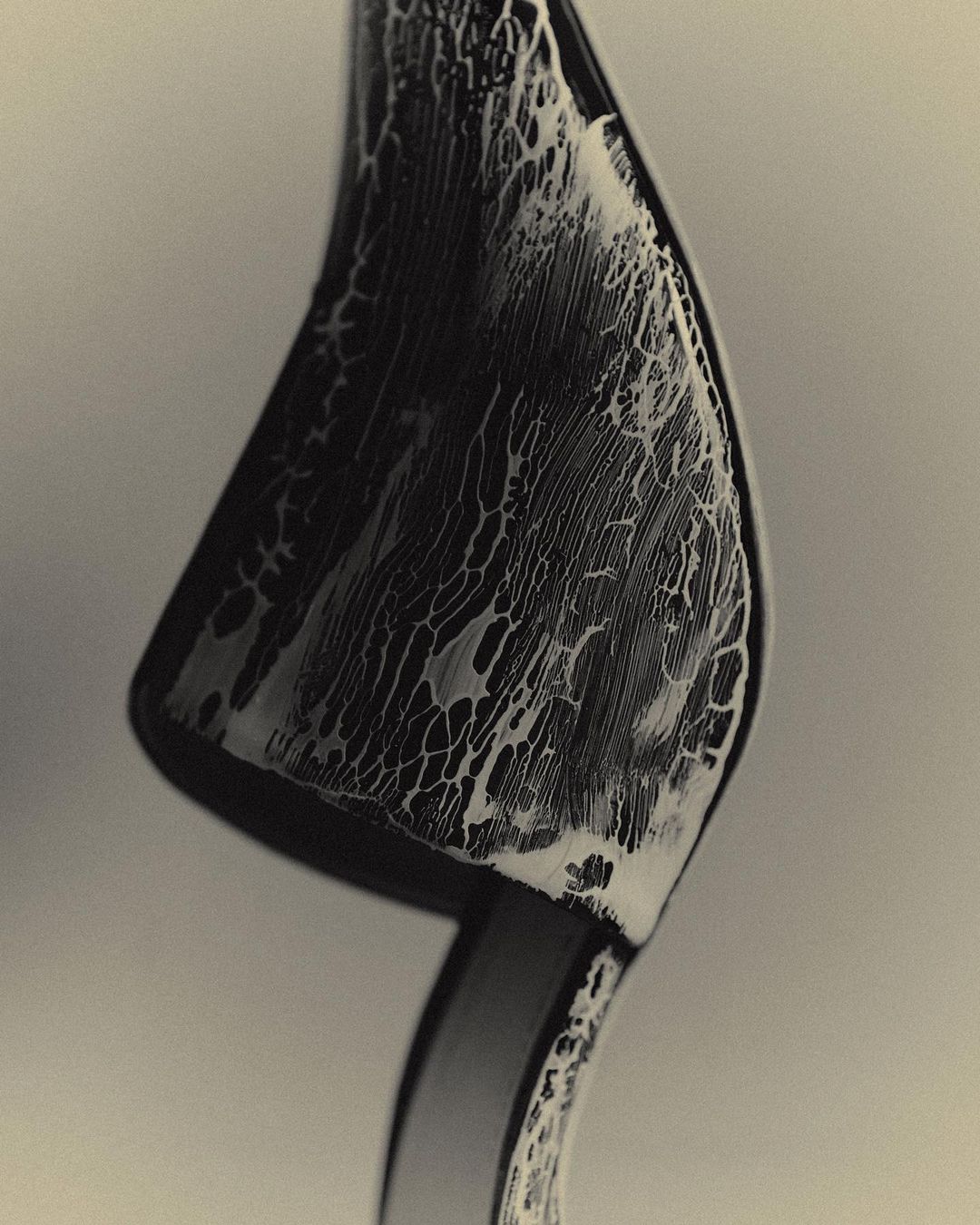 Close-up studio shot of a sleek black curved shoe with a textured white pattern, set against a graduated grey background.