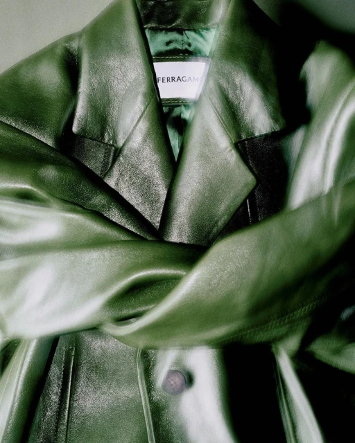 Close-up of a draped, olive green leather jacket with a 'Ferragamo' label, showcasing luxury fashion and craftsmanship in soft lighting.