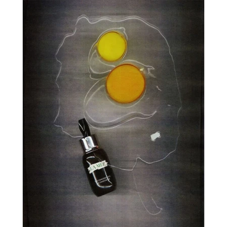 La Mer serum bottle positioned next to two raw egg yolks on a dark textured surface