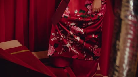 Close-up on floral-patterned red silk robe with red curtains in the background, vintage fashion photography, indoor scene.