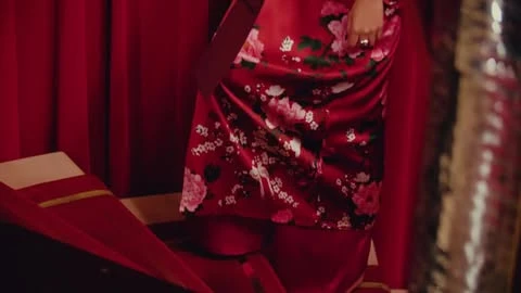 Close-up on floral-patterned red silk robe with red curtains in the background, vintage fashion photography, indoor scene.