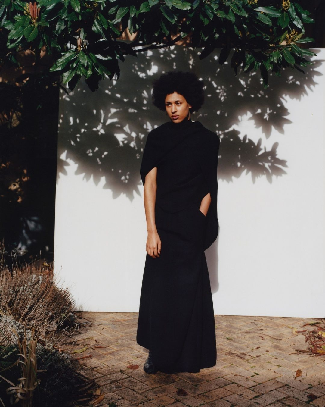 Model in black turtleneck and long skirt standing against a white backdrop with leaf shadows by photographer Joyce Ng