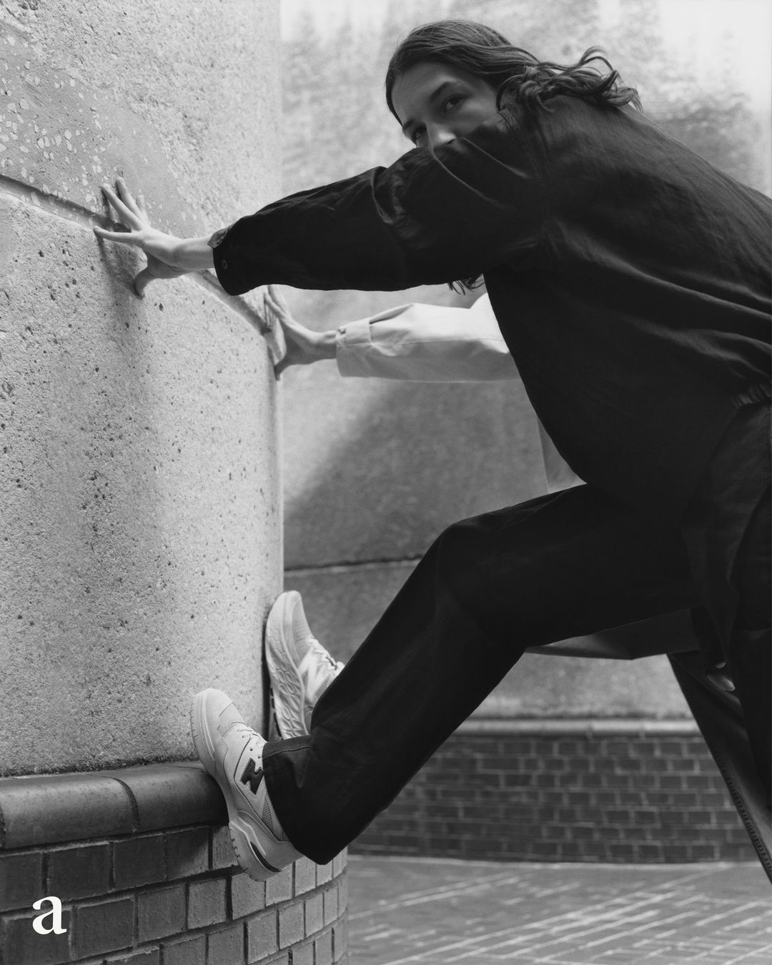 Monochrome shot of a person pushing against a concrete wall while wearing sneakers and dark clothing for a minimalist fashion look.