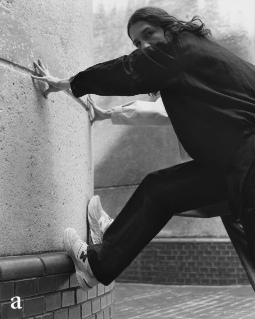 Monochrome shot of a person pushing against a concrete wall while wearing sneakers and dark clothing for a minimalist fashion look.