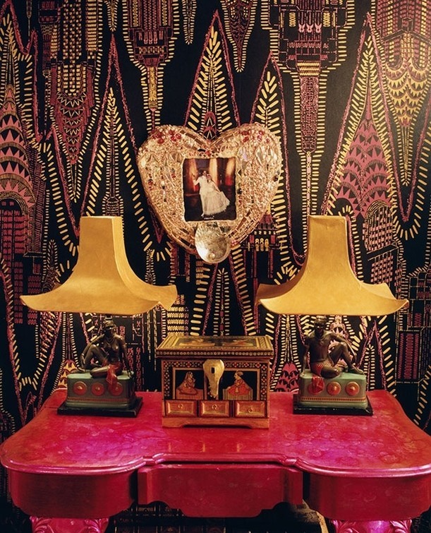 Decorative tabletop display featuring lamps, a jewelry box, and a heart-shaped frame against a graphic wallpaper backdrop.