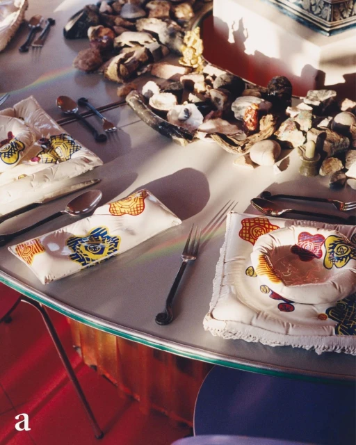 Stylized table setting featuring plates and flatware with unique patterned textiles and decorative rocks in a bright, indoor setting.