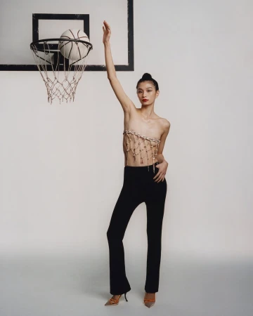 Model standing beneath a basketball hoop with her arm raised in a London studio portrait by Joyce Ng.