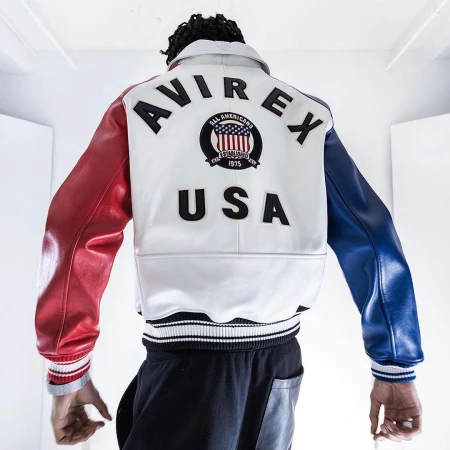 Rear view of a man wearing a red, white, and blue leather Avirex varsity jacket with USA lettering against a white background.