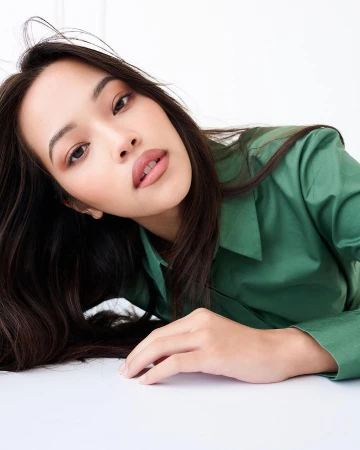 Portrait of a woman wearing a green shirt lying down against a white background by photographer Juan Algarin