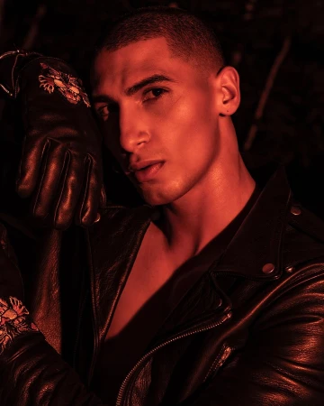 Man wearing a black leather jacket and leather glove, lit by moody red light in a portrait by Juan Algarin