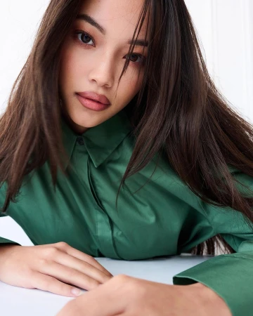 Close-up portrait of a woman with long dark hair wearing a green collared shirt against a white background