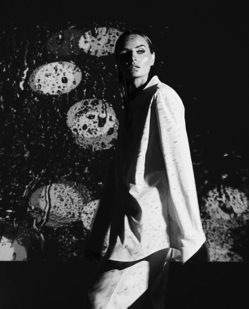 Monochrome portrait of a woman in an oversized button-down shirt against a projected background with oval bokeh shapes