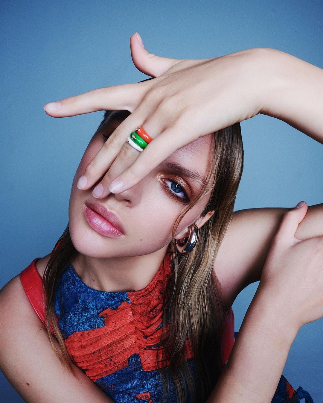Close-up portrait of a woman holding her hand across her face showcasing colorful rings and hoop earrings, photographed by Juan Algarin