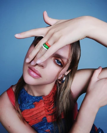 Close-up portrait of a woman holding her hand across her face showcasing colorful rings and hoop earrings, photographed by Juan Algarin