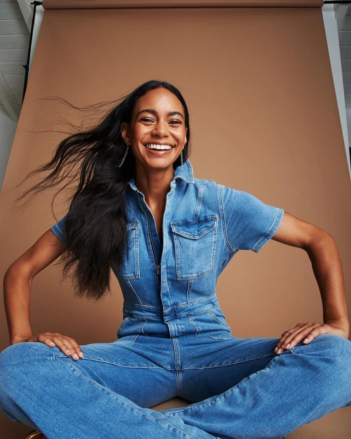 Smiling African American woman poses in a denim jumpsuit against a neutral background in a studio shot. Fashion and beauty portrait.