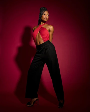 Elegant African American woman in a red wrap top and black wide-leg trousers, posing against a vibrant red backdrop in a studio setting.
