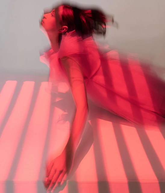Abstract blurred motion portrait of a woman in a dress with pink lighting, with horizontal light stripe pattern on a light background.