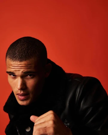 Close-up portrait of a man wearing a black leather jacket against a vibrant red backdrop photographed by Juan Algarin