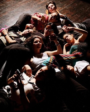 Overhead shot of a group of diverse young adults lying on the floor, some looking at their phones, in casual clothing and soft lighting.