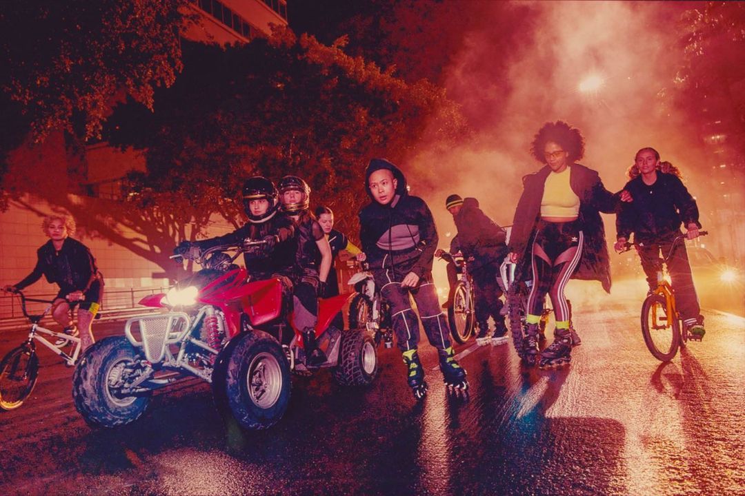 Group of young adults on a city street at night, riding ATVs, bikes, and rollerblades, illuminated by streetlights and car headlights.