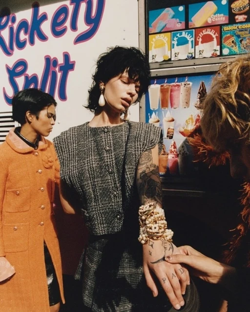Three women pose by a vintage ice cream truck, one with tattoos and heavy pearl bracelets, in a fashion editorial with an urban backdrop.