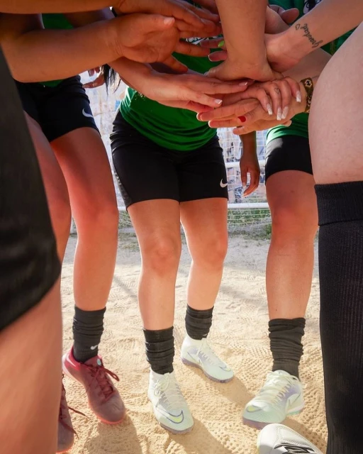 Close-up of a group of female athletes in green and black uniforms with their hands stacked together, creating a sense of unity.