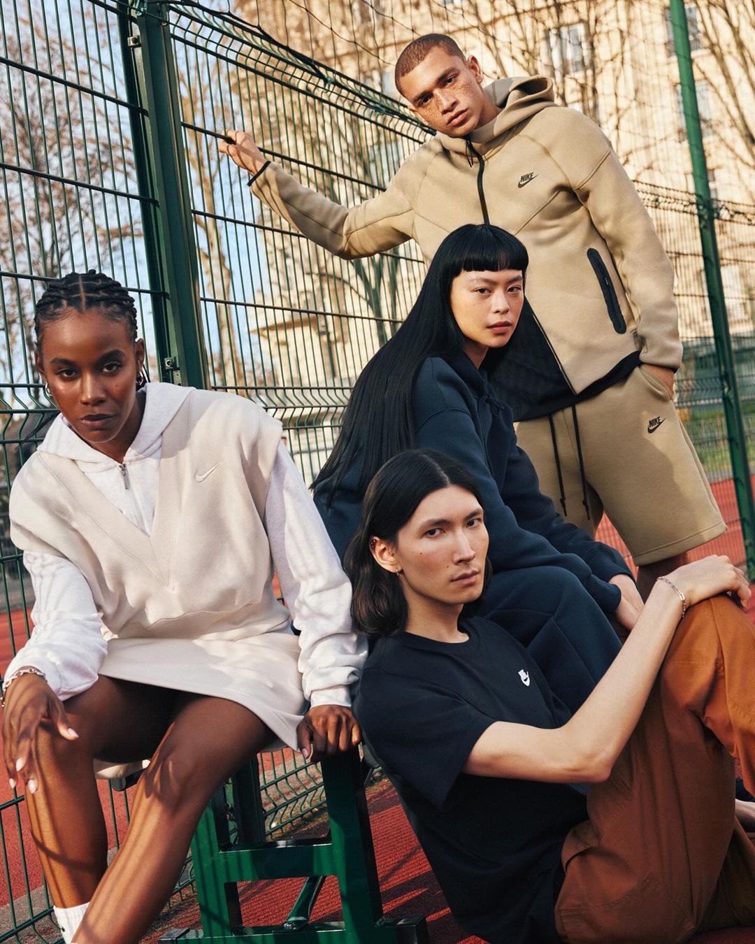 Four diverse young adult models pose together outdoors in activewear. They are wearing apparel with the Nike logo in a daylight shot.