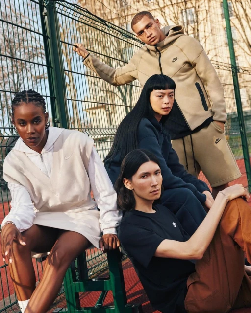 Four diverse young adult models pose together outdoors in activewear. They are wearing apparel with the Nike logo in a daylight shot.