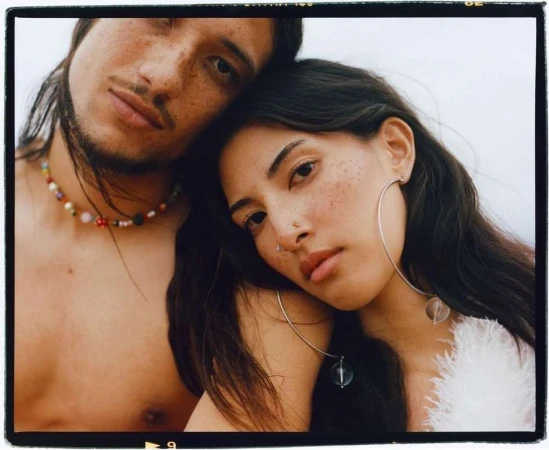 Close-up portrait of a young couple posing together with their heads touching against an overcast sky background.