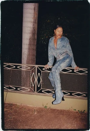 Woman in denim jacket and matching denim boots seated on an ornate railing at night outdoors