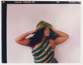 Portrait of a woman wearing a green striped top and a fuzzy green hat against a seamless white background.