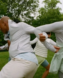 Group of people in light-coloured athletic apparel linking arms outdoors in a park by Juanita Richards