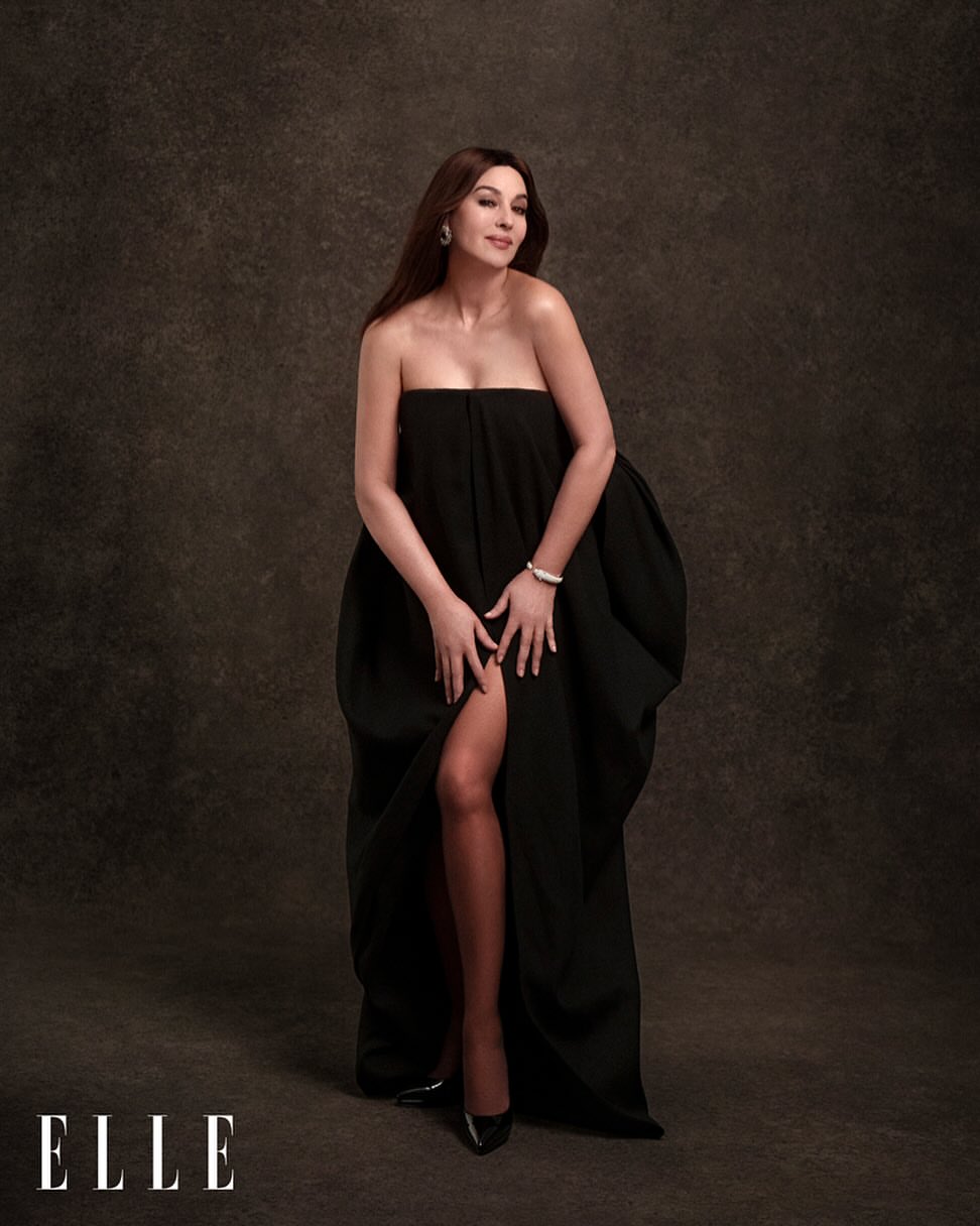 Monica Bellucci poses in a black dress against a textured brown background, with 'ELLE' logo visible in the lower-left corner.