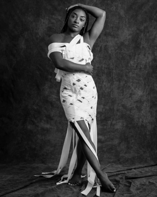 Monochromatic portrait of a barefoot African-American woman in a wrapped dress, posing against a textured backdrop in a photo studio.
