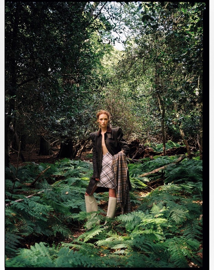 Fashion photography in outdoor wooded setting with a standing young woman in jacket, skirt, boots and scarf.
