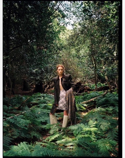 Fashion photography in outdoor wooded setting with a standing young woman in jacket, skirt, boots and scarf.