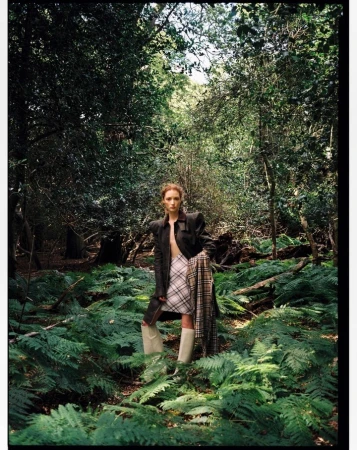 Fashion photography in outdoor wooded setting with a standing young woman in jacket, skirt, boots and scarf.