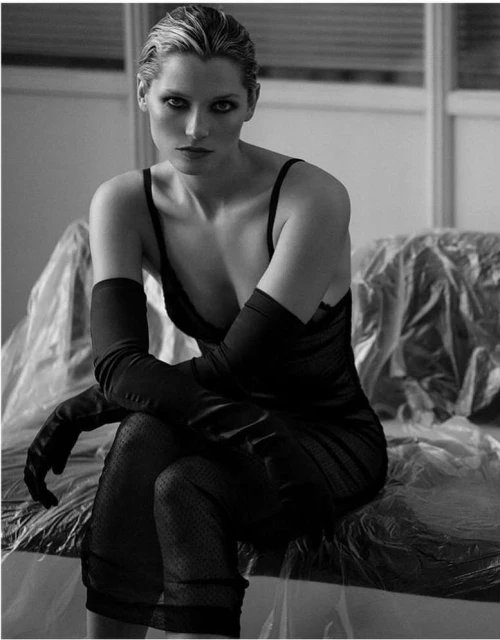 Monochrome portrait of a woman wearing a black dress and long gloves, seated indoors with muted lighting, conveying a serious expression.
